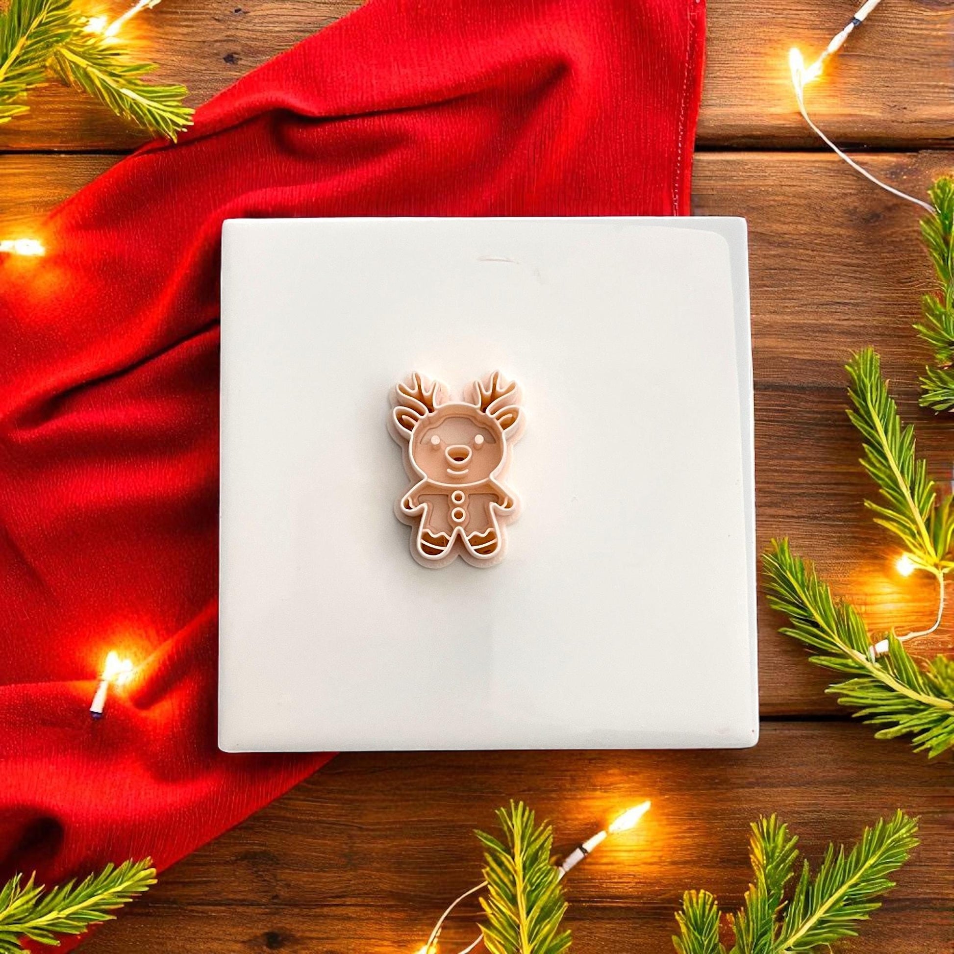 Gingerbread reindeer polymer clay cutter on red background surrounded by Christmas lights