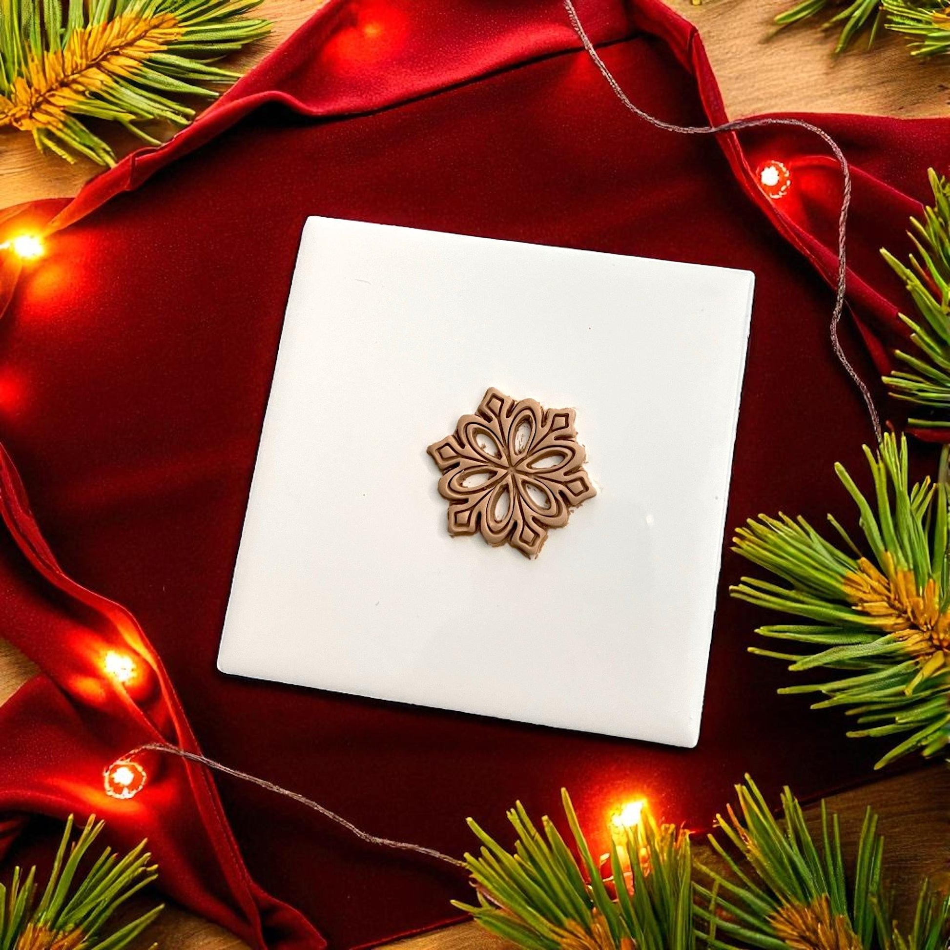 Small snowflake clay design centered on white tile with red cloth and greenery