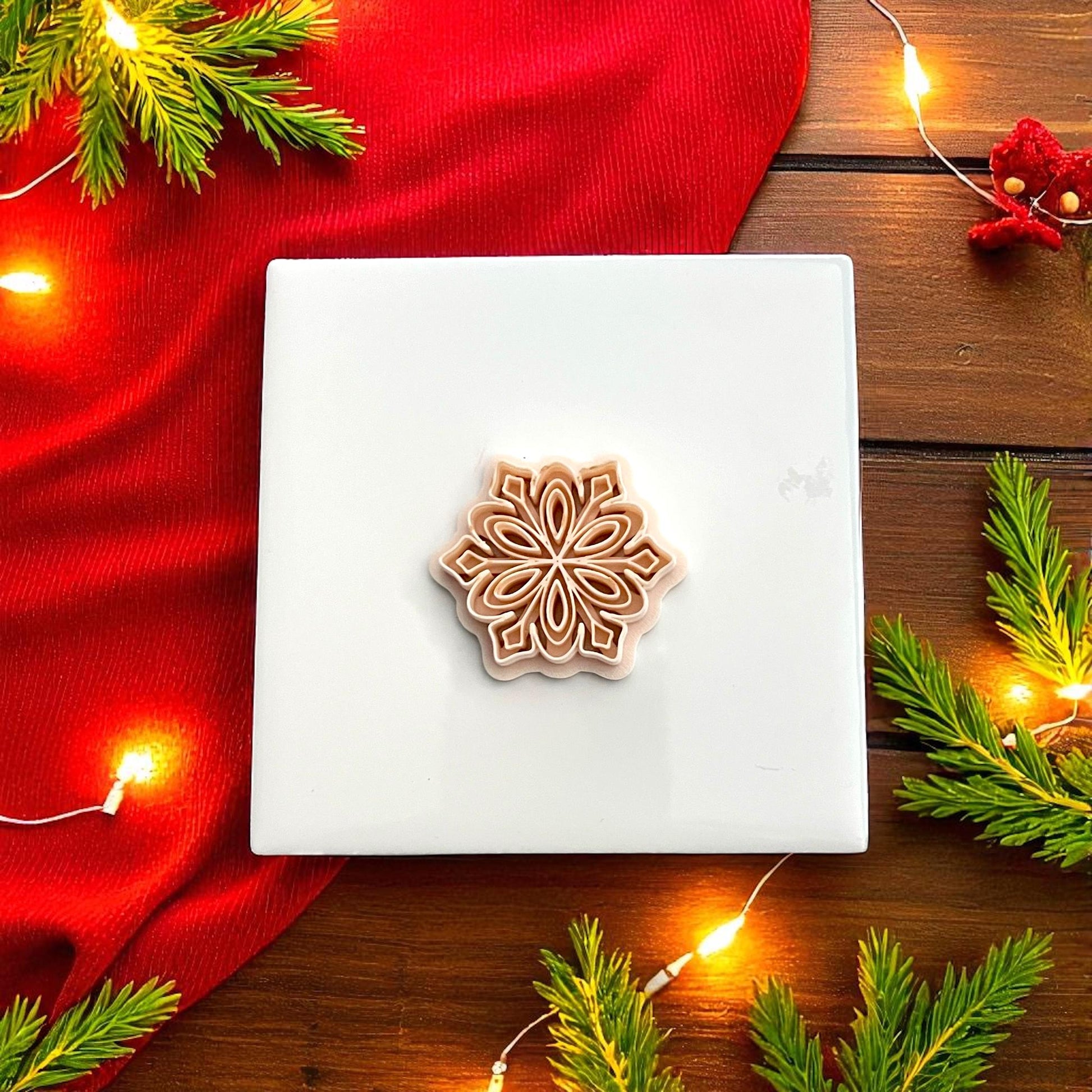 Polymer clay snowflake cutter on white tile surrounded by pine greenery and red fabric