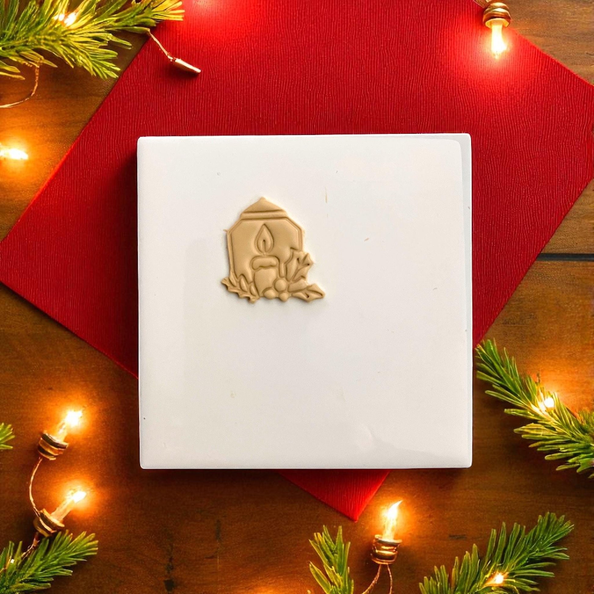 Candle and cutter side by side on white tile surrounded by Christmas lights and pine