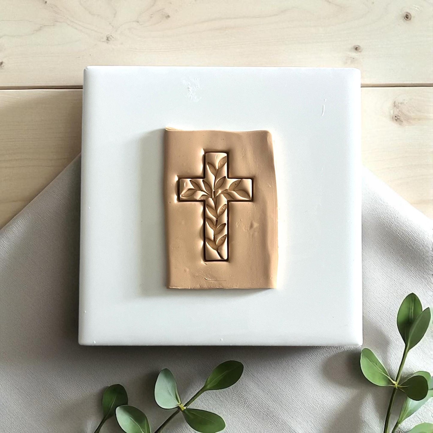Ivy cross clay impression on white tile with eucalyptus leaves