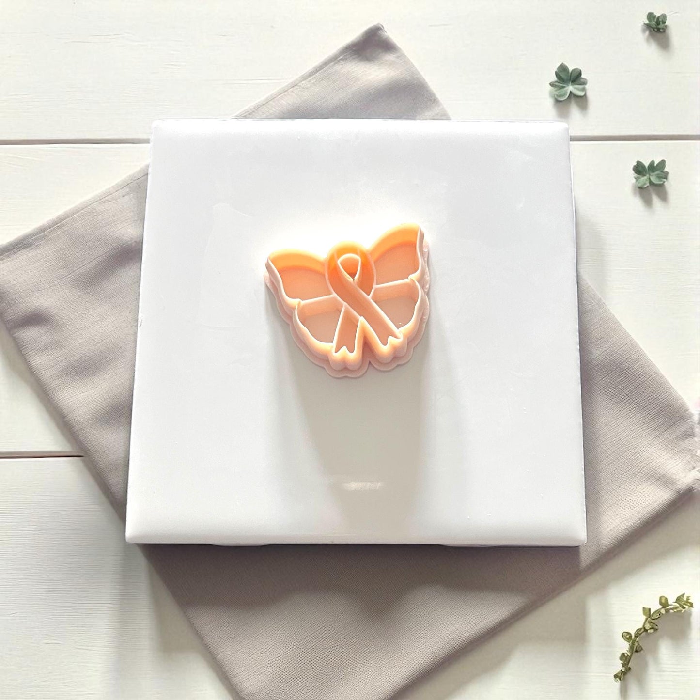 Close-up of butterfly ribbon clay impression surrounded by leaves