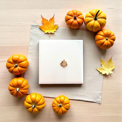 Small turkey clay impression on white tile surrounded by pumpkins and autumn decor