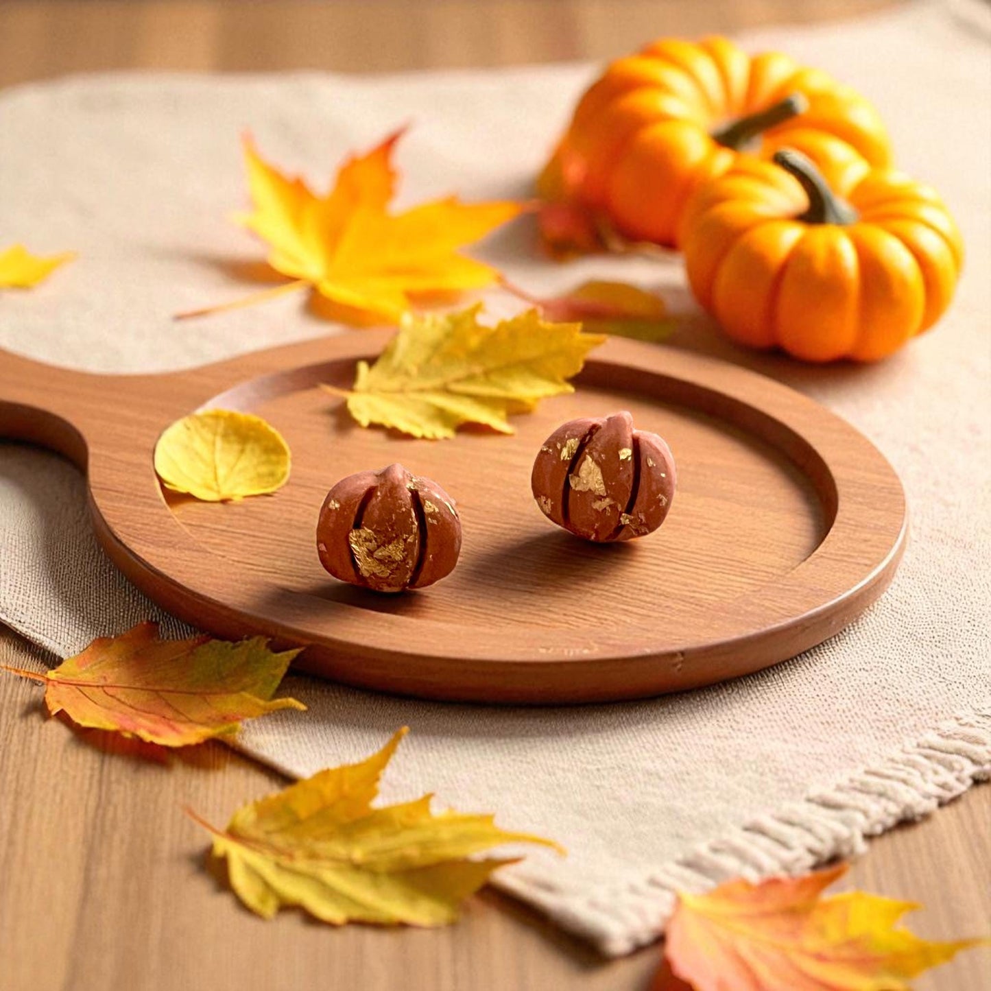 Pumpkin polymer clay earrings with gold detail on wooden plate and fall leaves