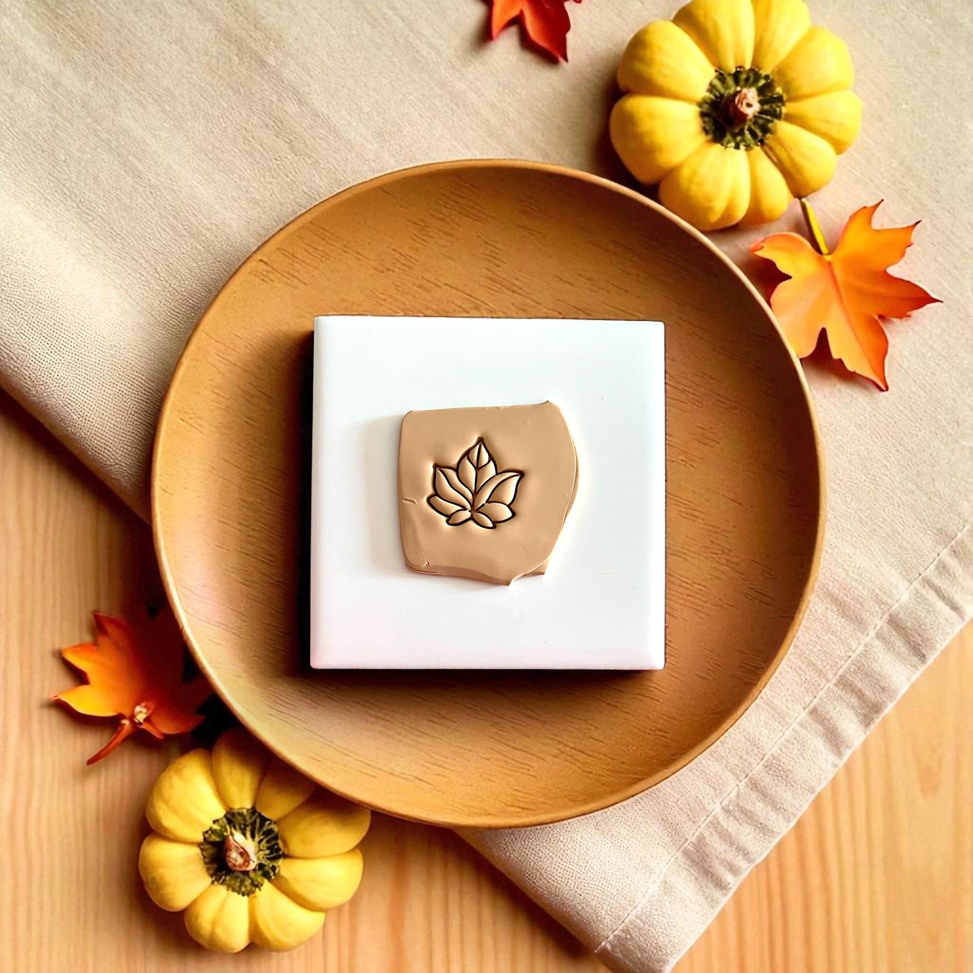 Autumn leaf polymer clay piece on wooden plate surrounded by small pumpkins and yellow leaves