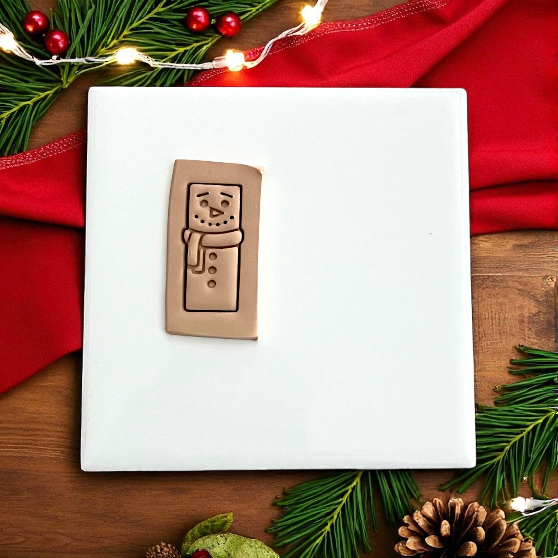 Snowman bar polymer clay cutter displayed on white tile with red holiday fabric and pine branches