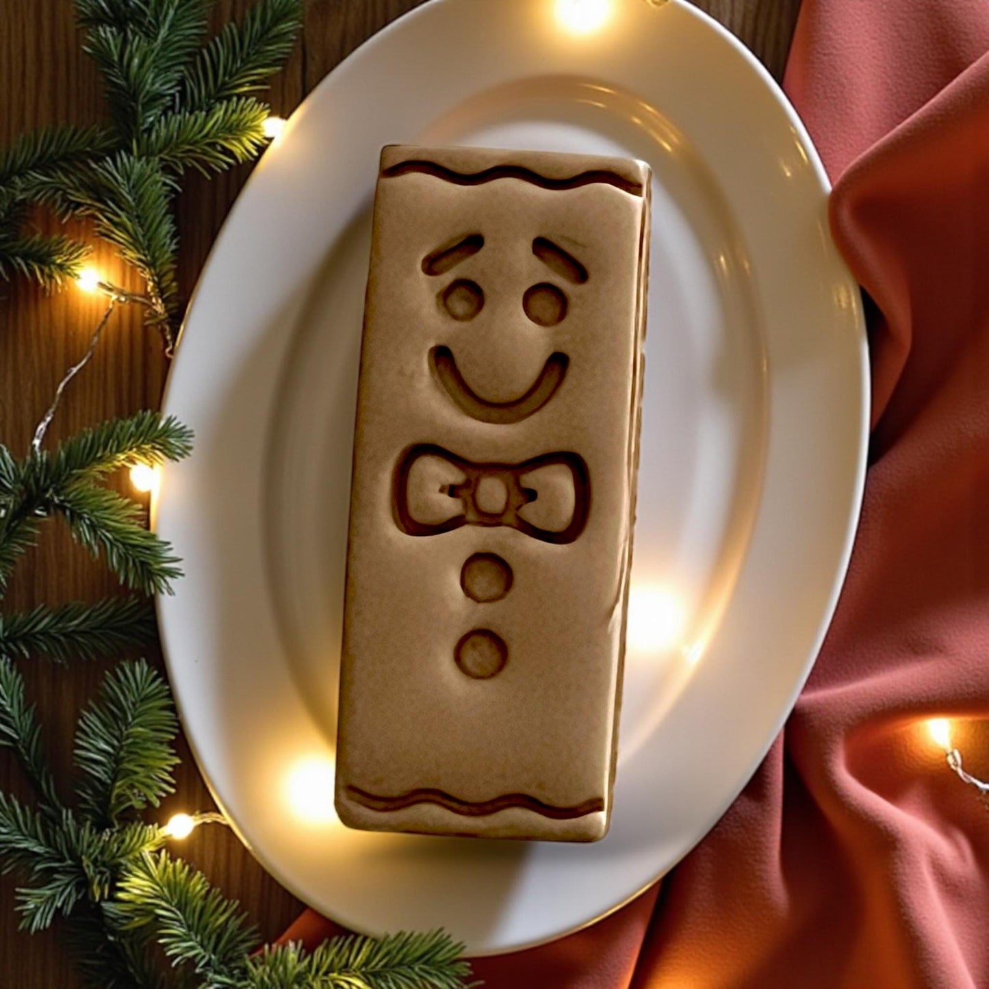 Large gingerbread bar clay design on plate surrounded by holiday lights and pine