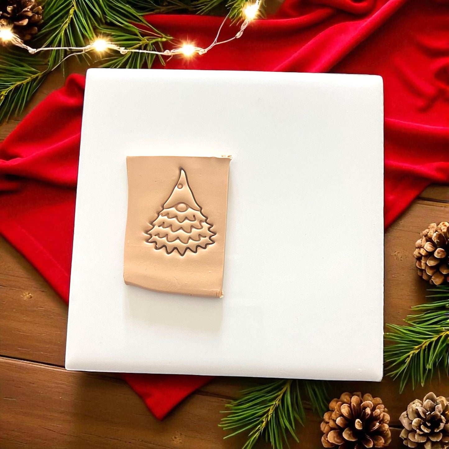 Gnome tree clay impression pressed into clay on white tile with pinecones and red cloth