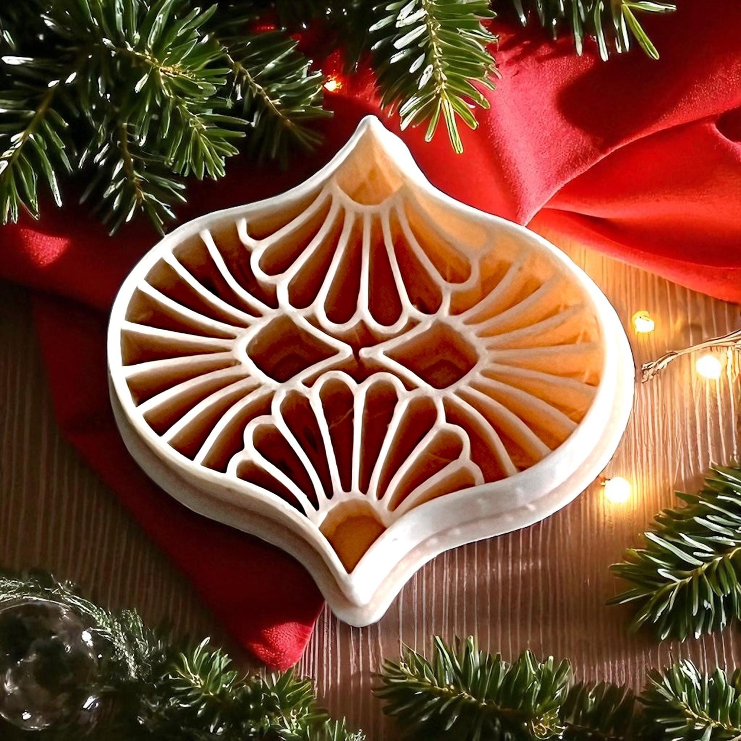 detailed ornament polymer clay cutter on red fabric with pine branches and lights