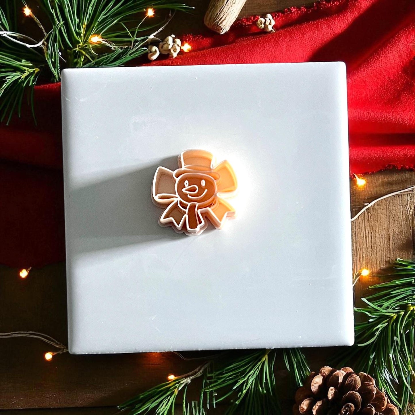 Polymer clay snowman bow cutter displayed on white tile with Christmas greenery