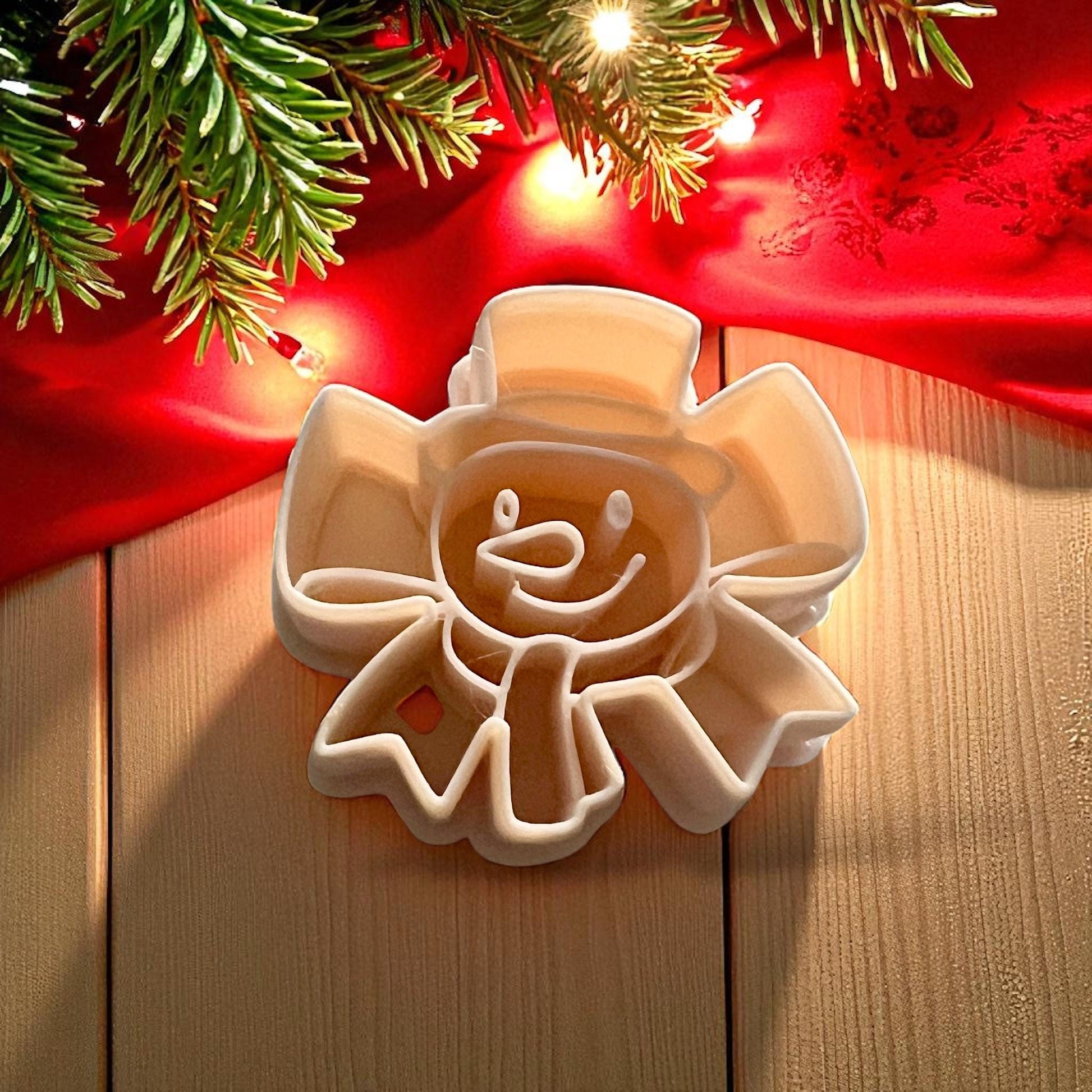 Snowman ribbon bow polymer clay cutter on wooden surface with red cloth and holiday lights