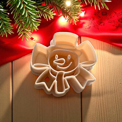 Snowman ribbon bow polymer clay cutter on wooden surface with red cloth and holiday lights