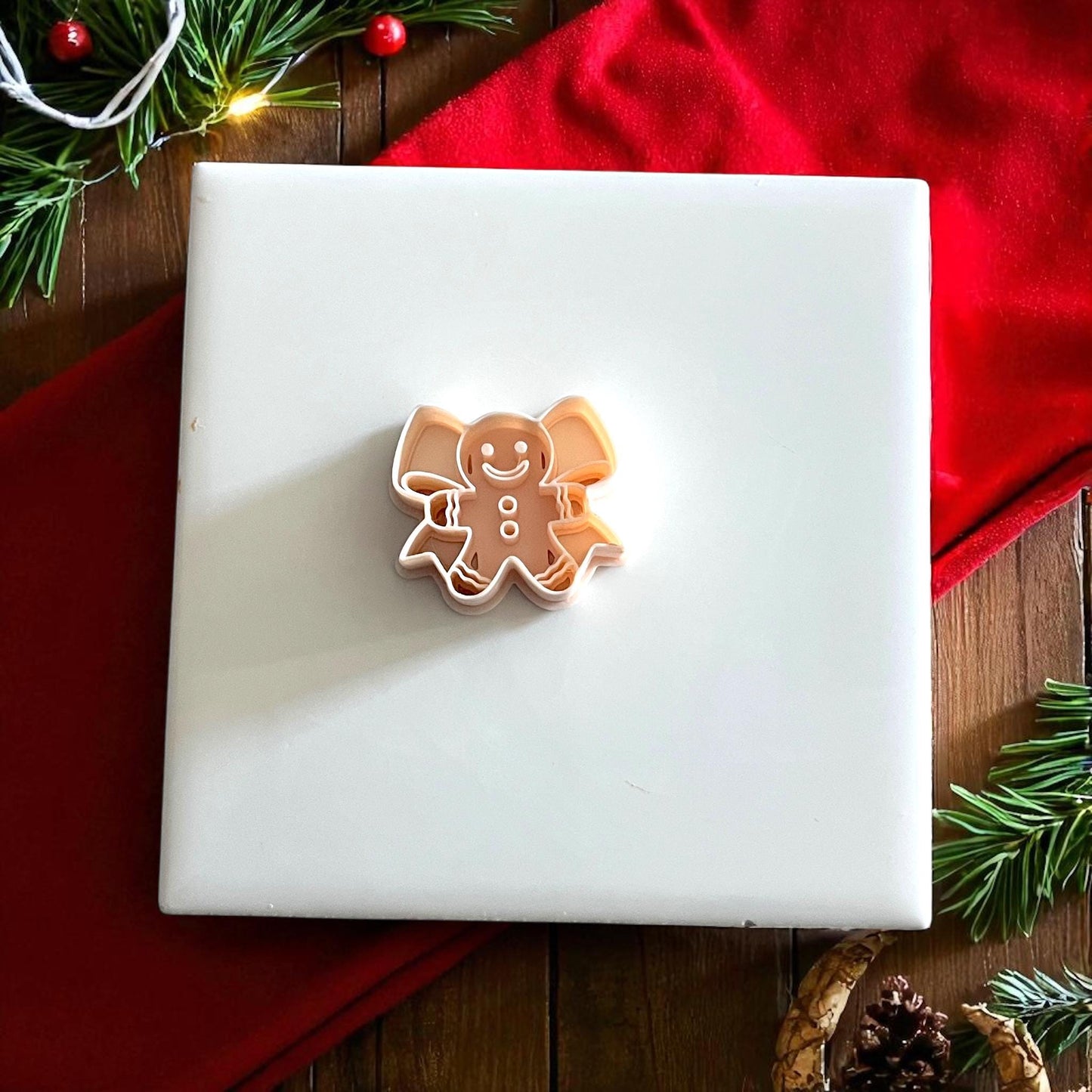 Gingerbread bow polymer clay cutter on white tile with red cloth and holiday greenery
