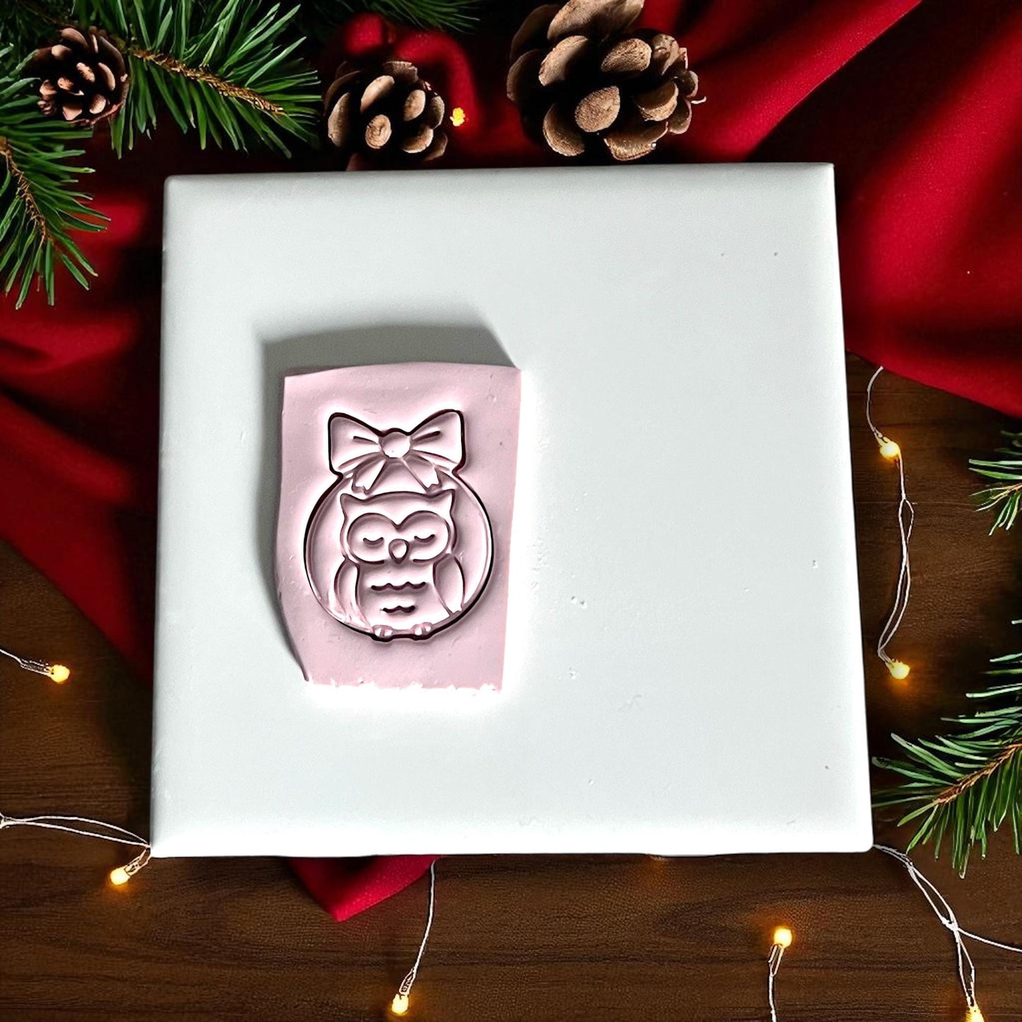 Pink clay imprint of owl ornament with bow on white tile