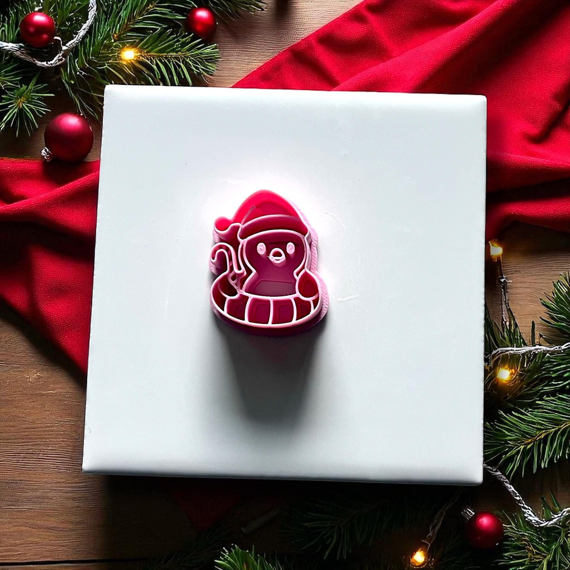 Pink penguin floatie polymer clay cutter on white tile with greenery