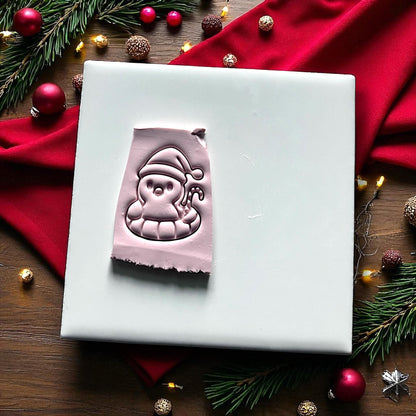 Pink clay imprint of penguin in floatie with Santa hat and candy cane