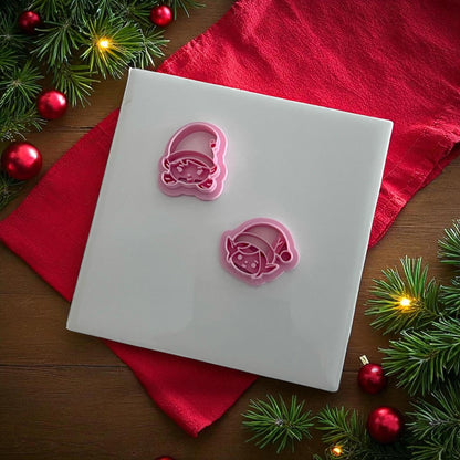 Two Christmas elf face polymer clay cutters on white tile with red fabric and ornaments