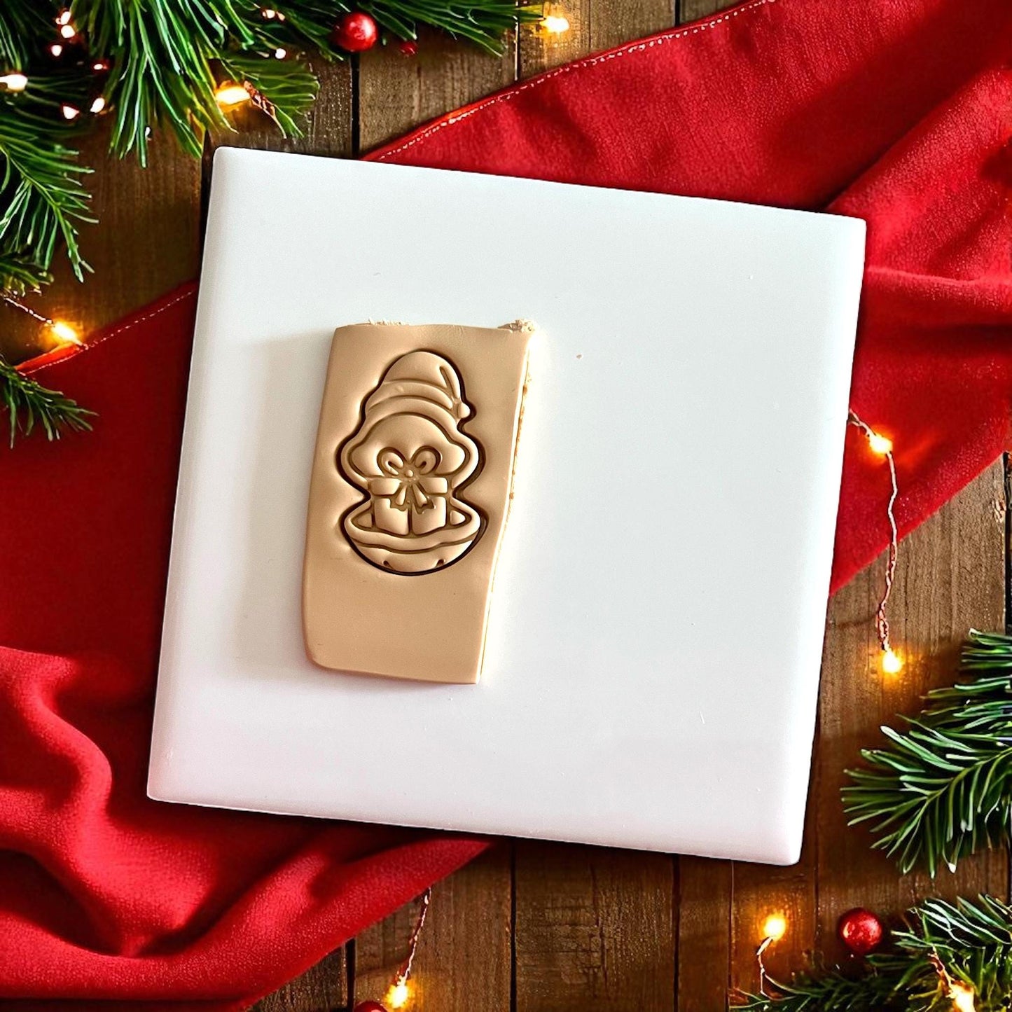 Square clay slab with oyster and present impression surrounded by holiday greenery