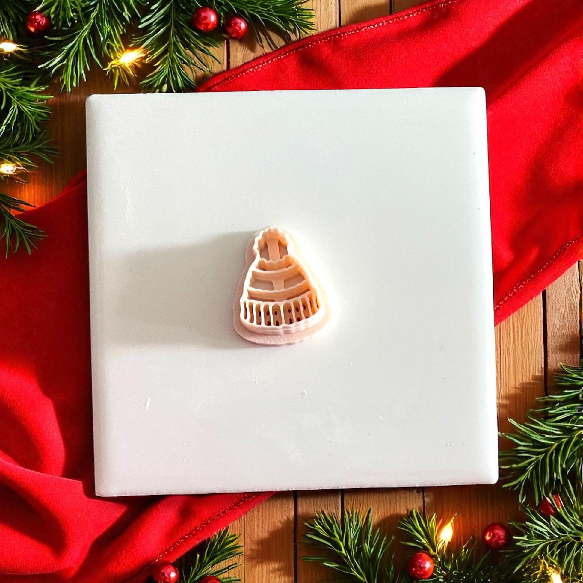 Polymer clay beanie impression on tile surrounded by Christmas greenery and red fabric
