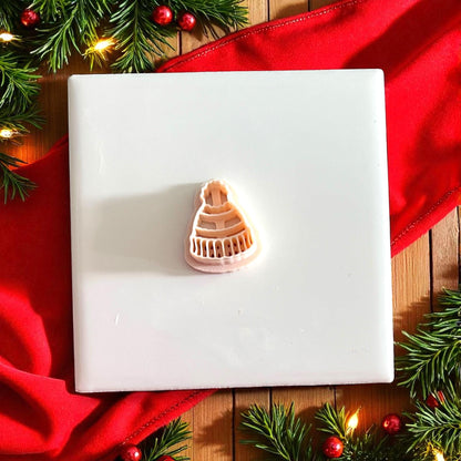 Polymer clay beanie impression on tile surrounded by Christmas greenery and red fabric