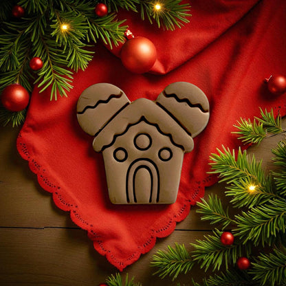 Large gingerbread mouse house clay impression on red cloth surrounded by pine branches and ornaments