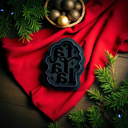 Black Fa La La polymer clay cutter displayed on red fabric with pine branches