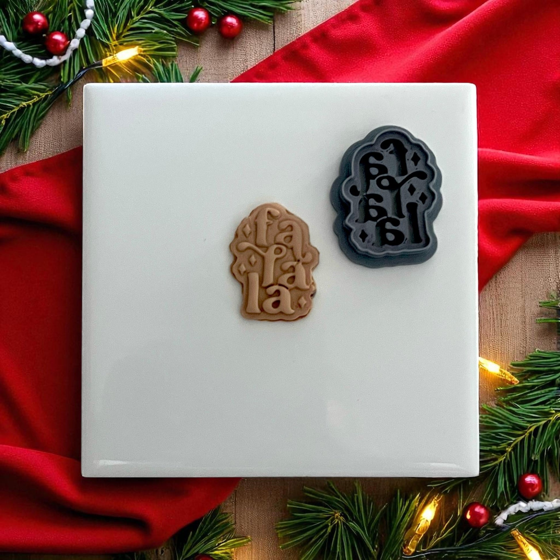 Fa La La polymer clay cutter and impression on white tile with red Christmas backdrop