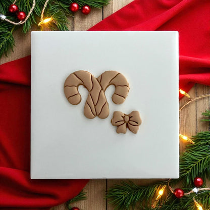 Candy cane bow clay design on white tile surrounded by Christmas lights and greenery