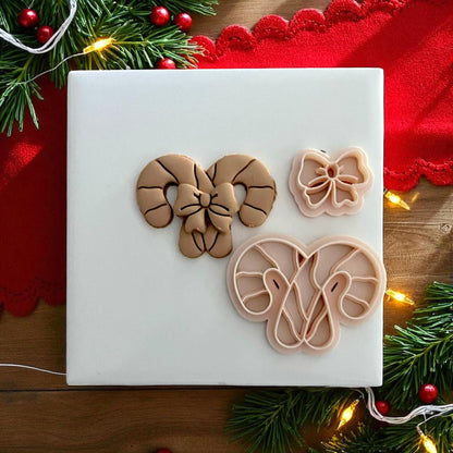 Candy cane bow polymer clay cutters displayed on red fabric with pine branches and ornaments