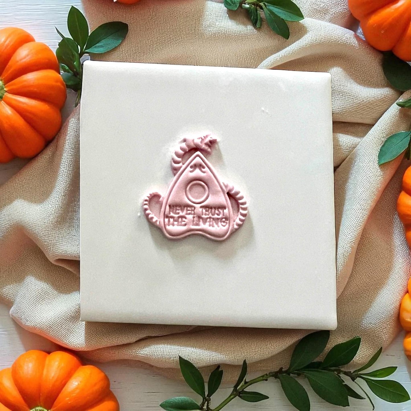 Pink clay imprint of Never Trust the Living planchette with pumpkins around