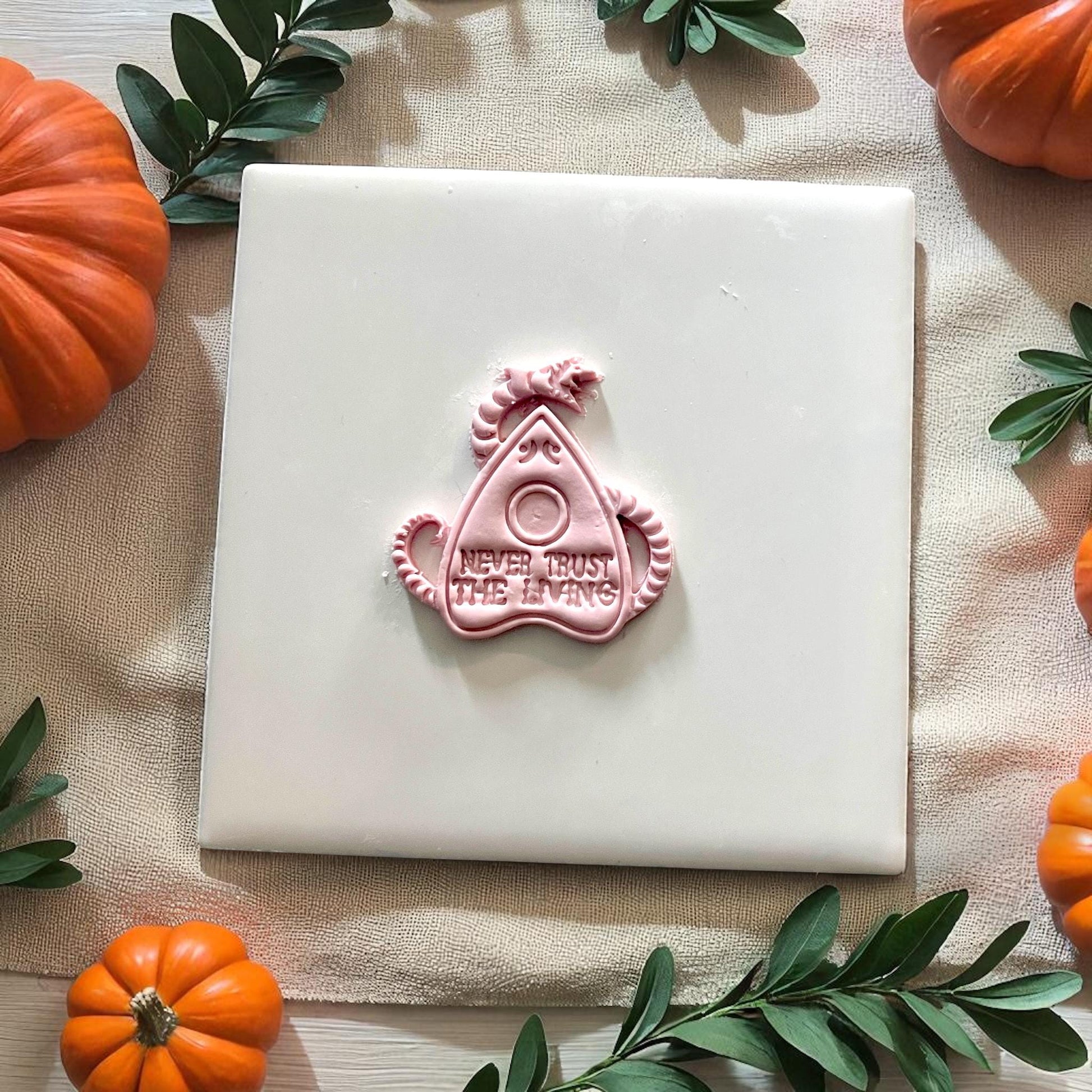 Clay imprint of planchette cutter with Never Trust the Living phrase