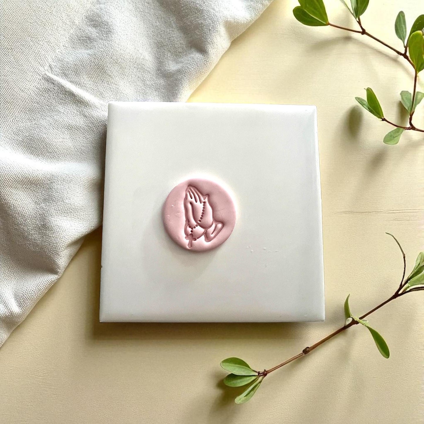 Small praying hands with rosary clay imprint on white tile with flowers
