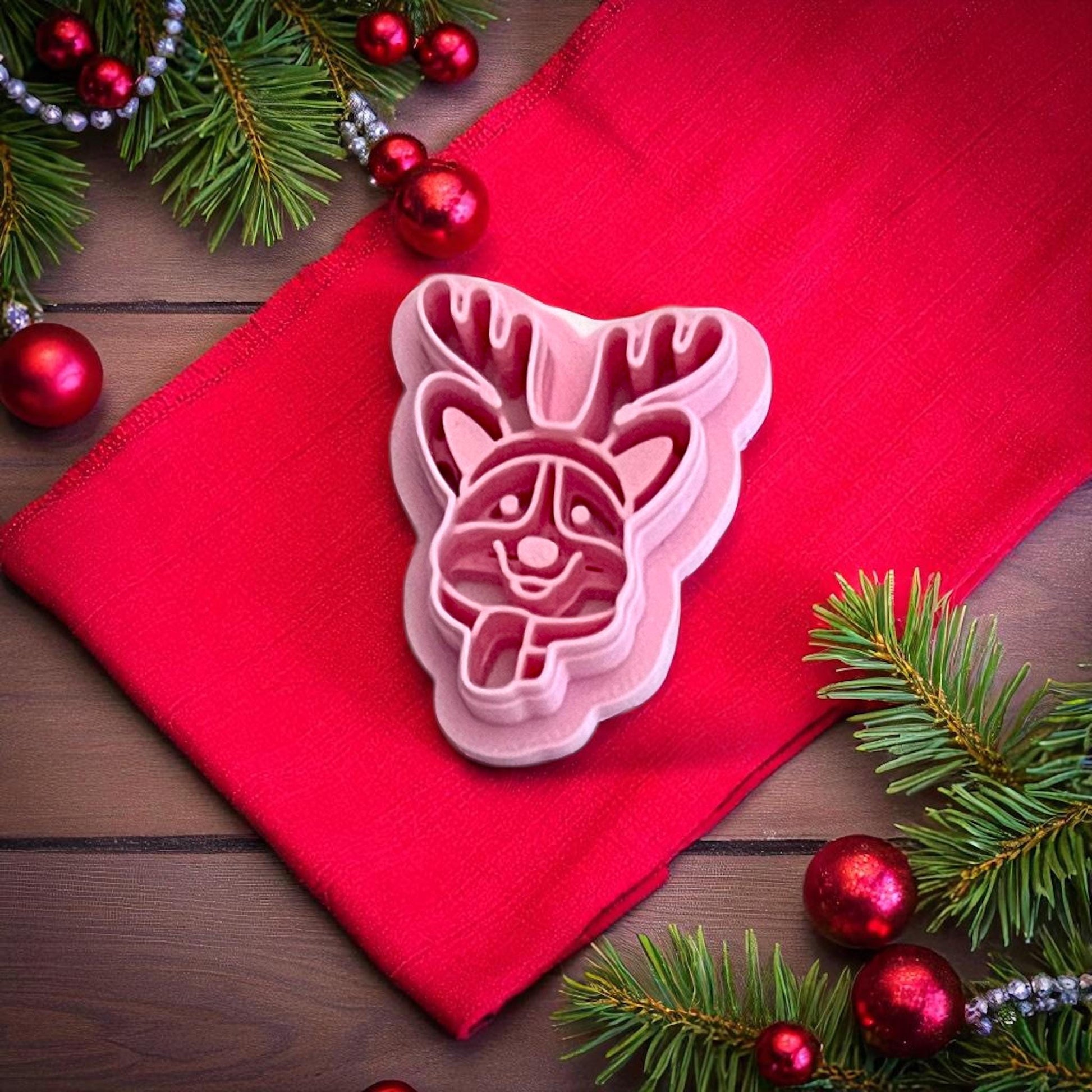 Pink polymer clay cutter shaped like corgi dog with reindeer antlers displayed on red fabric