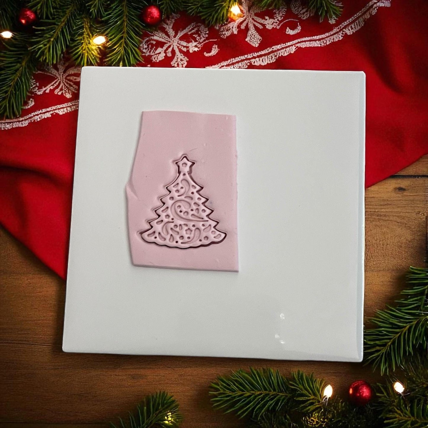 Pink clay imprint of swirly Christmas tree polymer clay cutter on white tile with red cloth