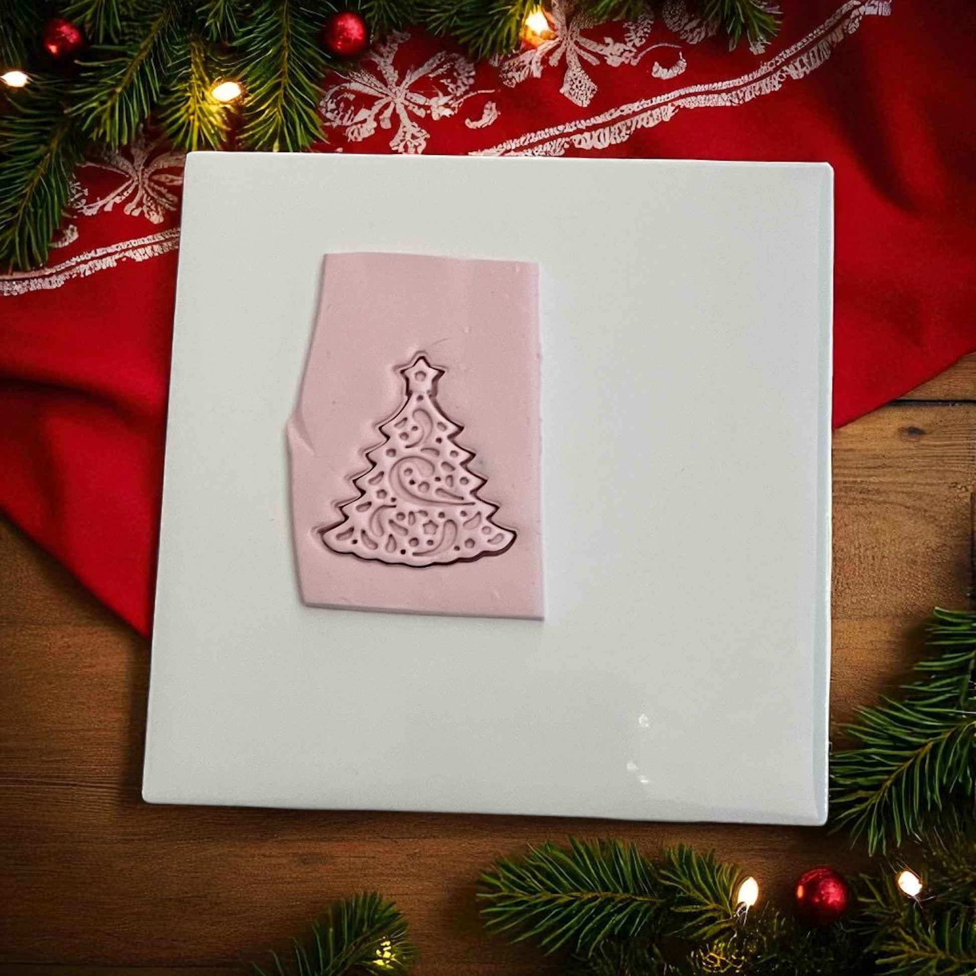 Pink clay imprint of swirly Christmas tree polymer clay cutter on white tile with red cloth
