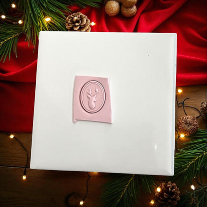 Pink clay imprint of oval reindeer silhouette polymer clay cutter on white tile with Christmas greenery