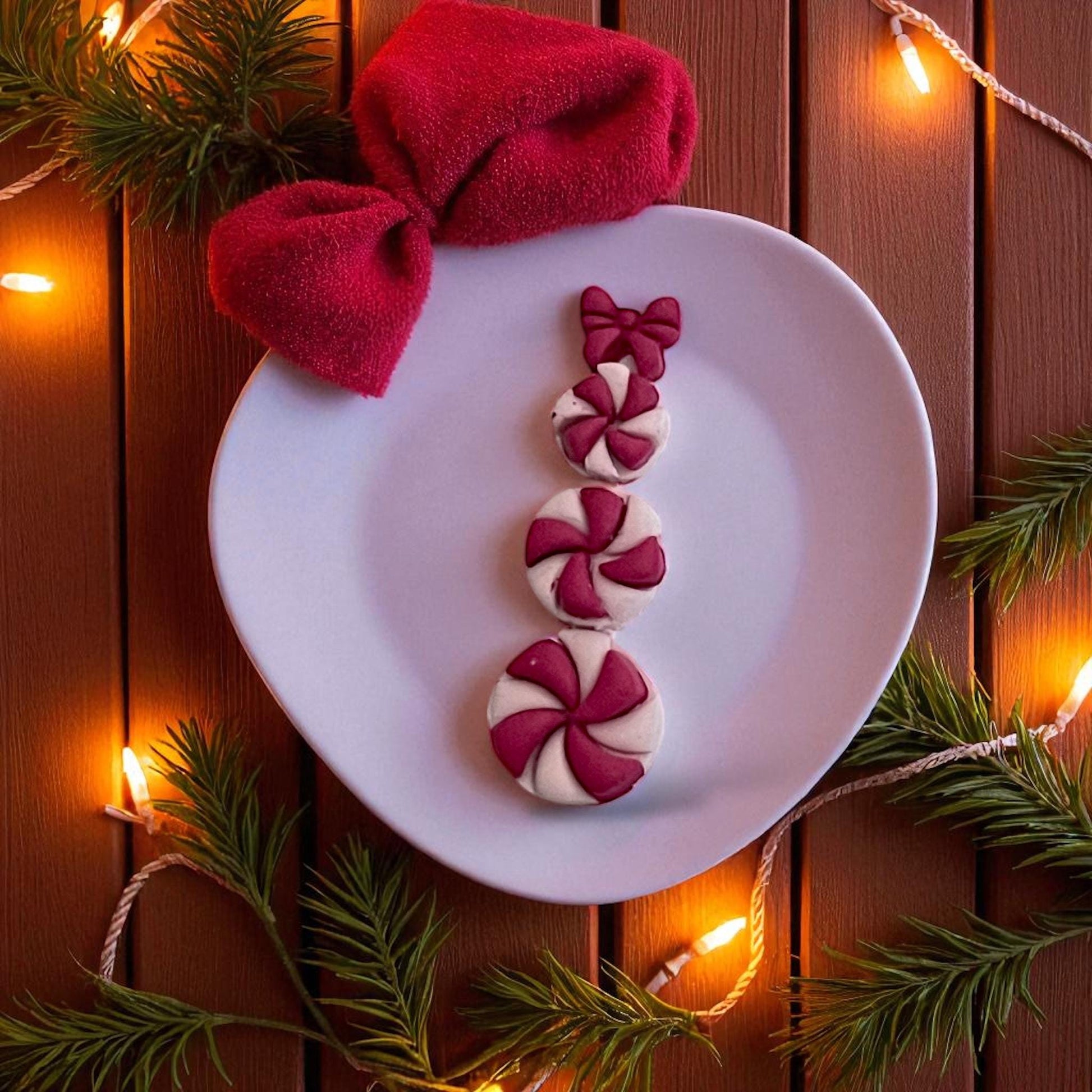 Peppermint candy snowman clay pieces with bow on plate surrounded by Christmas lights