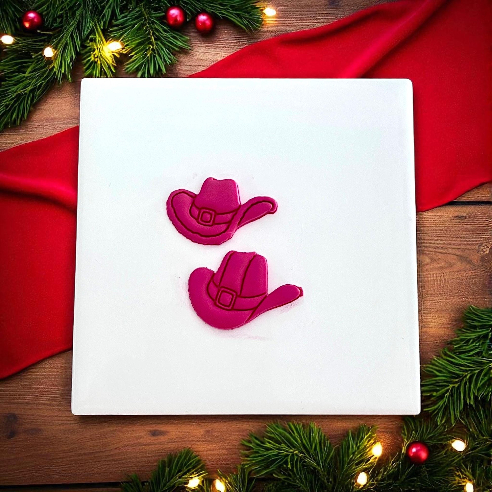 Holiday Santa cowboy hat clay shapes on white tile surrounded by Christmas greenery