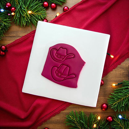 Red clay impressions of Mr and Mrs Santa cowboy hats on white tile with festive decor