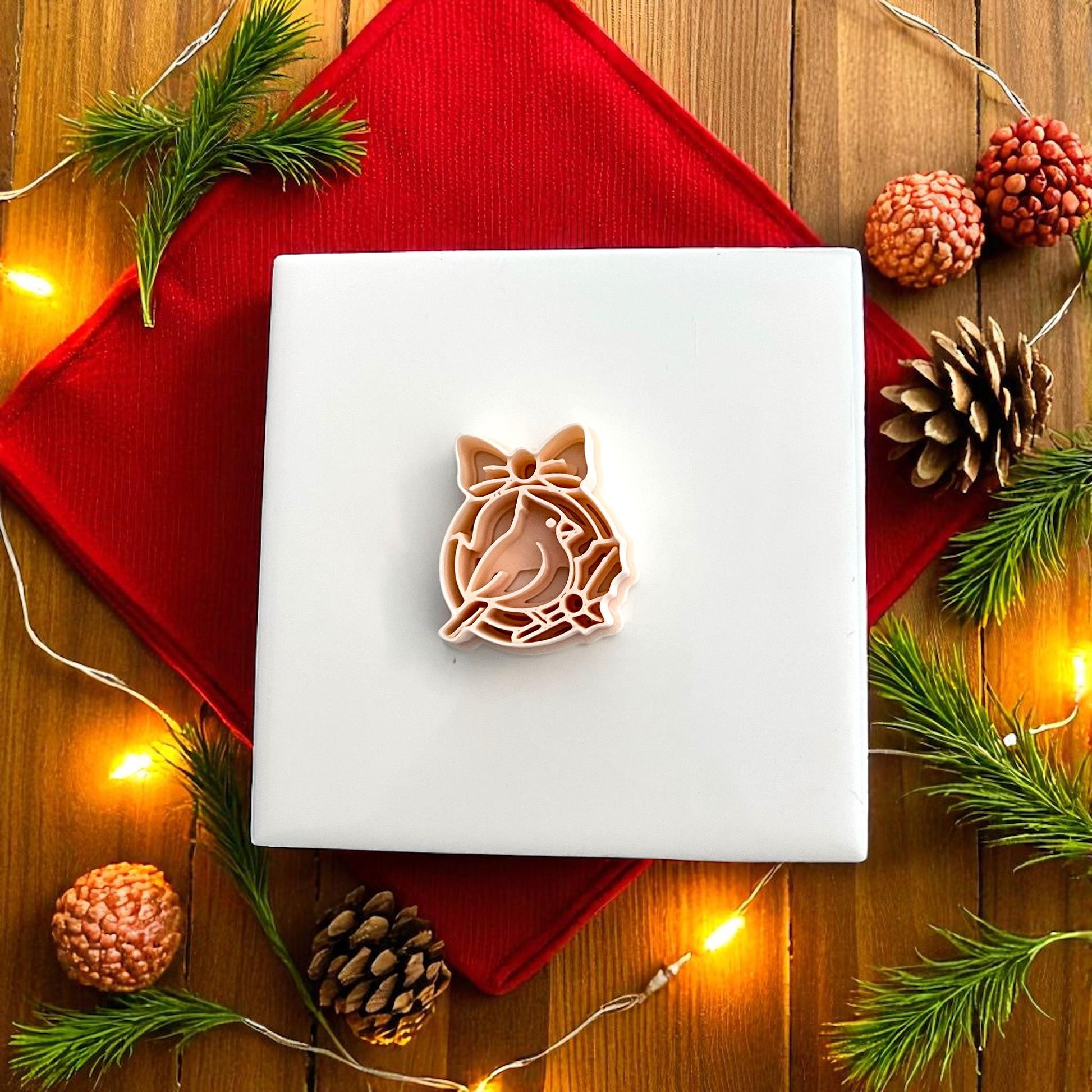 Polymer clay cutter shaped like cardinal ornament surrounded by pine and holiday lights
