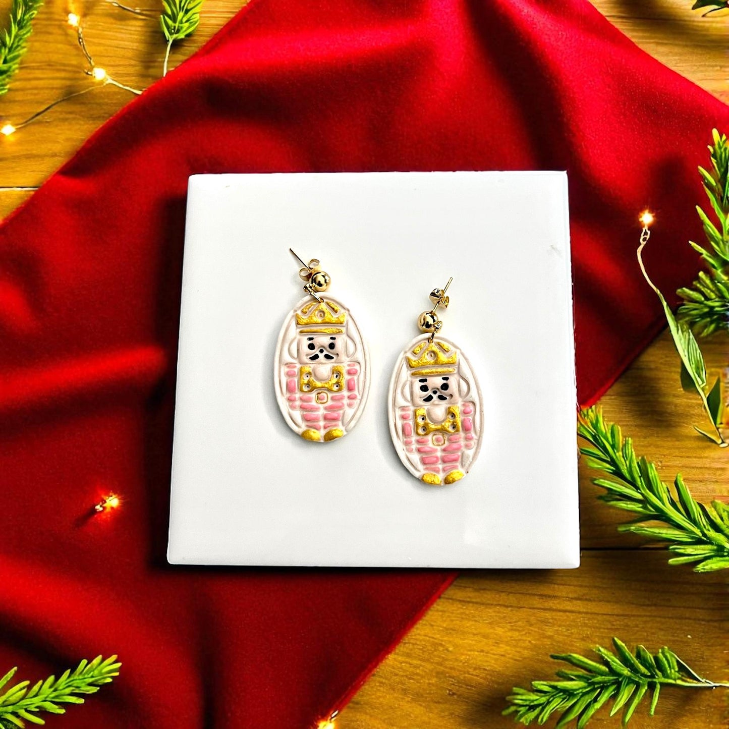 Finished nutcracker clay earrings painted gold and pink displayed on white tile