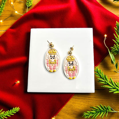 Finished nutcracker clay earrings painted gold and pink displayed on white tile
