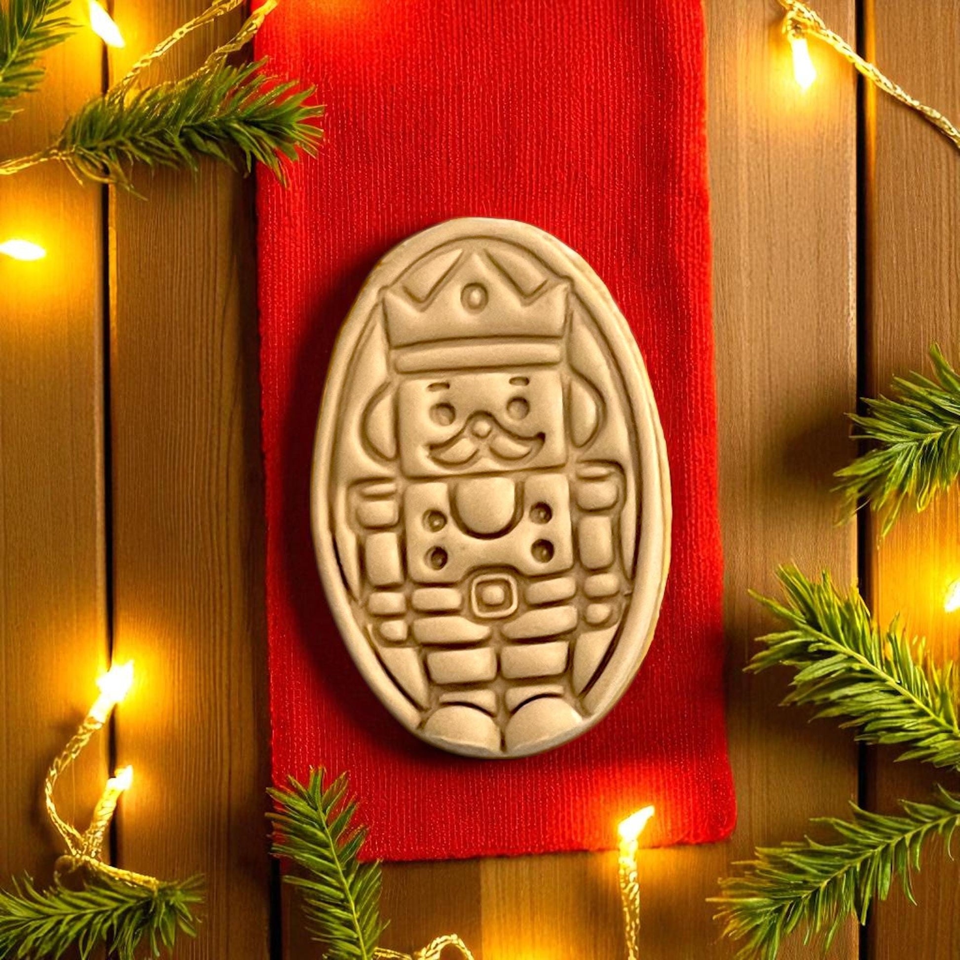 Holiday nutcracker clay impression on red ribbon surrounded by pine and lights