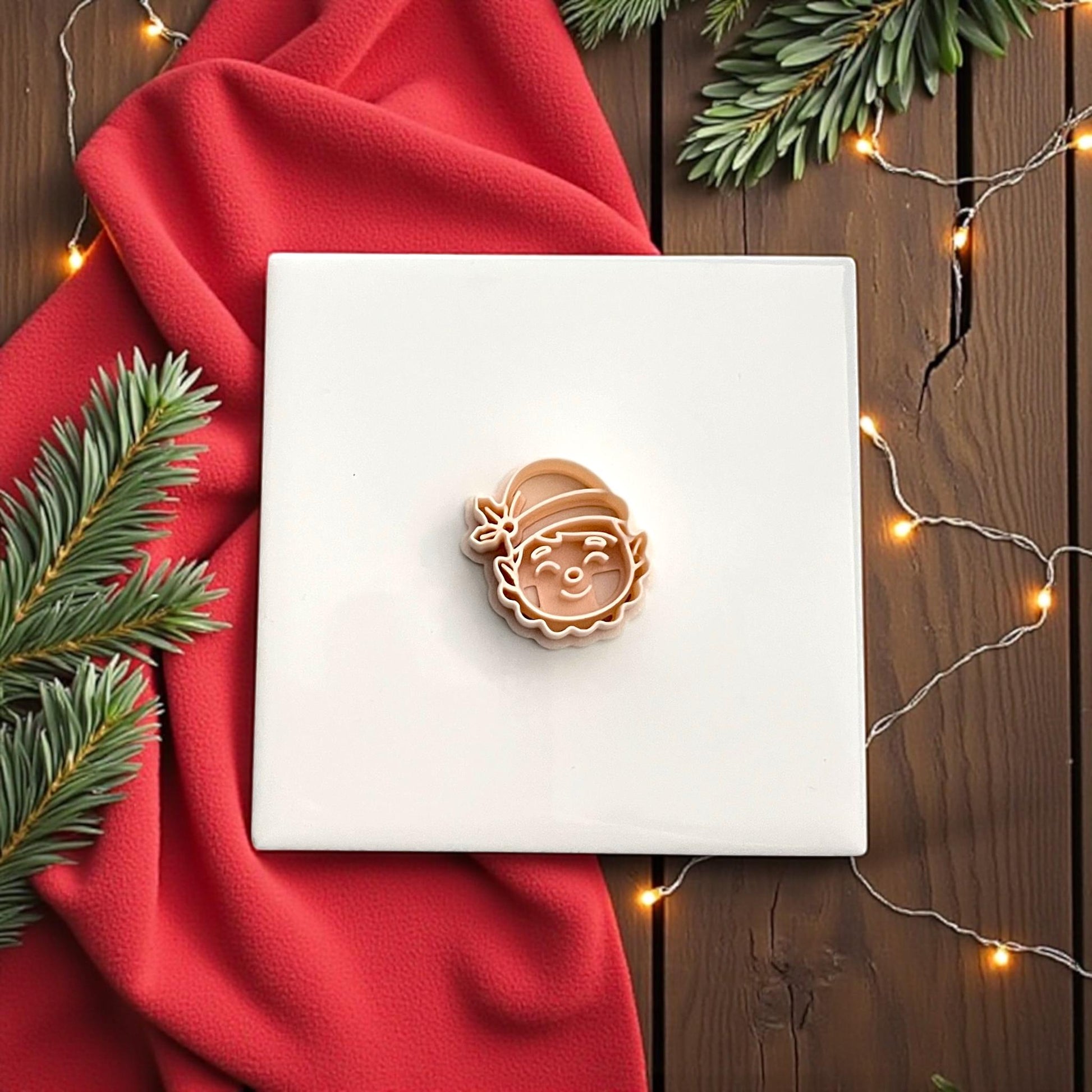 Elf face polymer clay cutter on red background with festive greenery