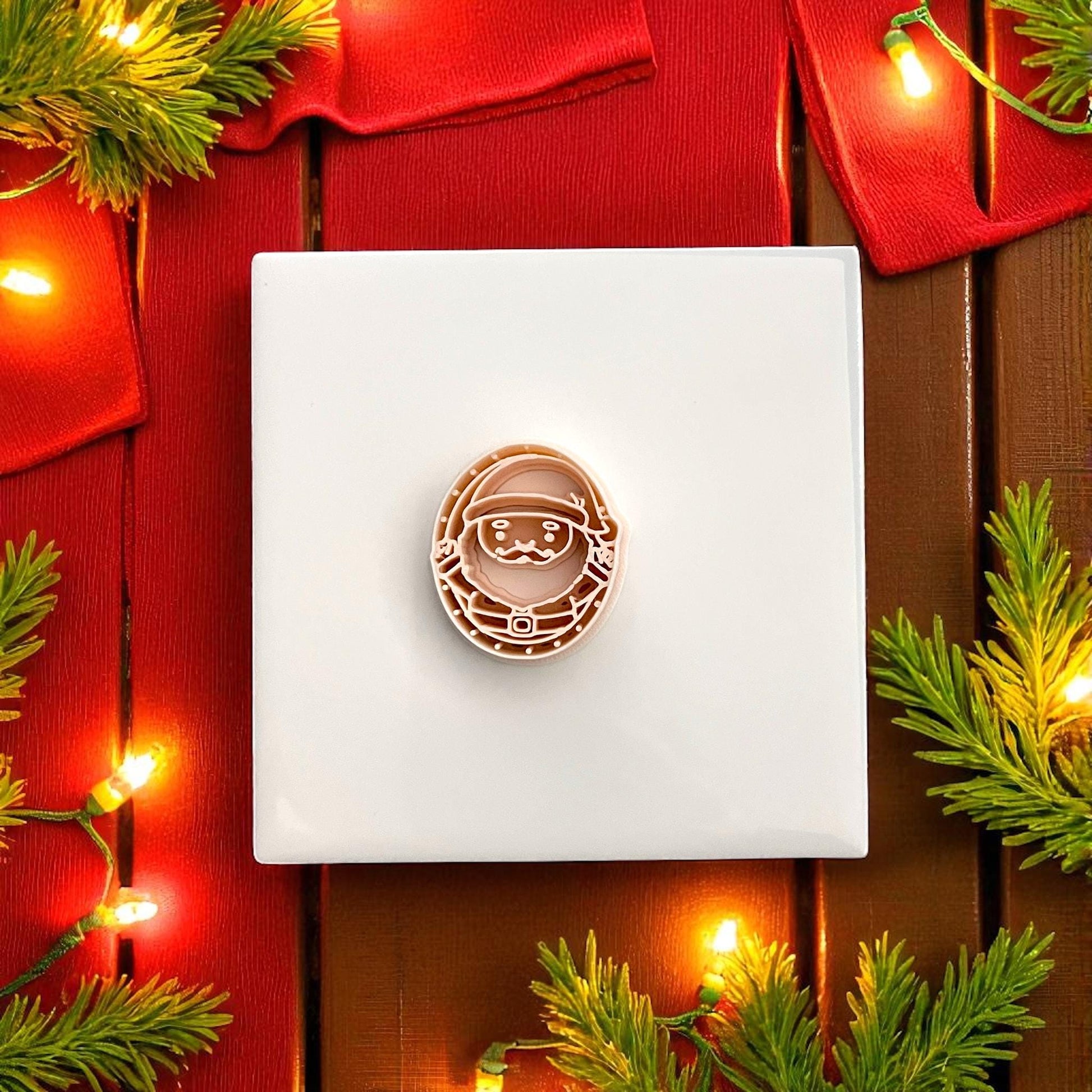 Santa face polymer clay cutter on red background surrounded by greenery and lights
