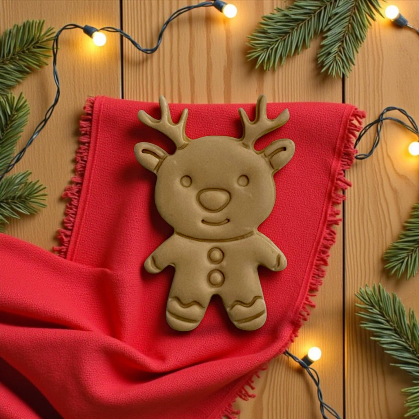 Large gingerbread reindeer clay imprint on red fabric with string lights and pine sprigs