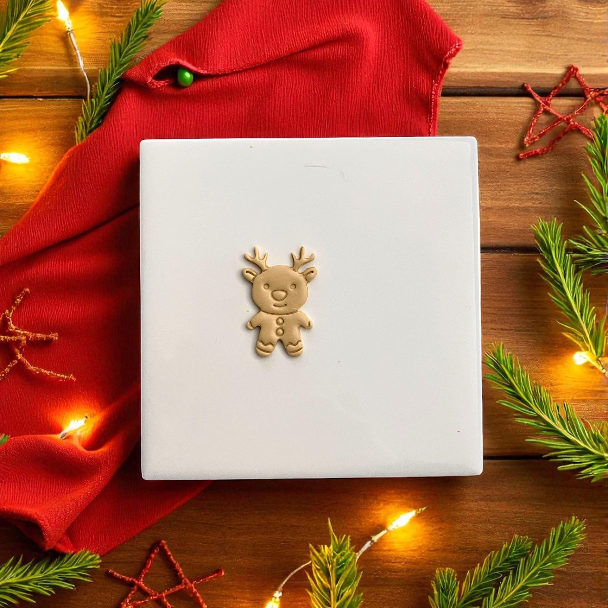 Small gingerbread reindeer imprint on white tile with red background and pine decor