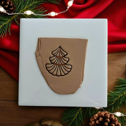 Scalloped Christmas tree clay impression pressed into tan clay sheet on white tile