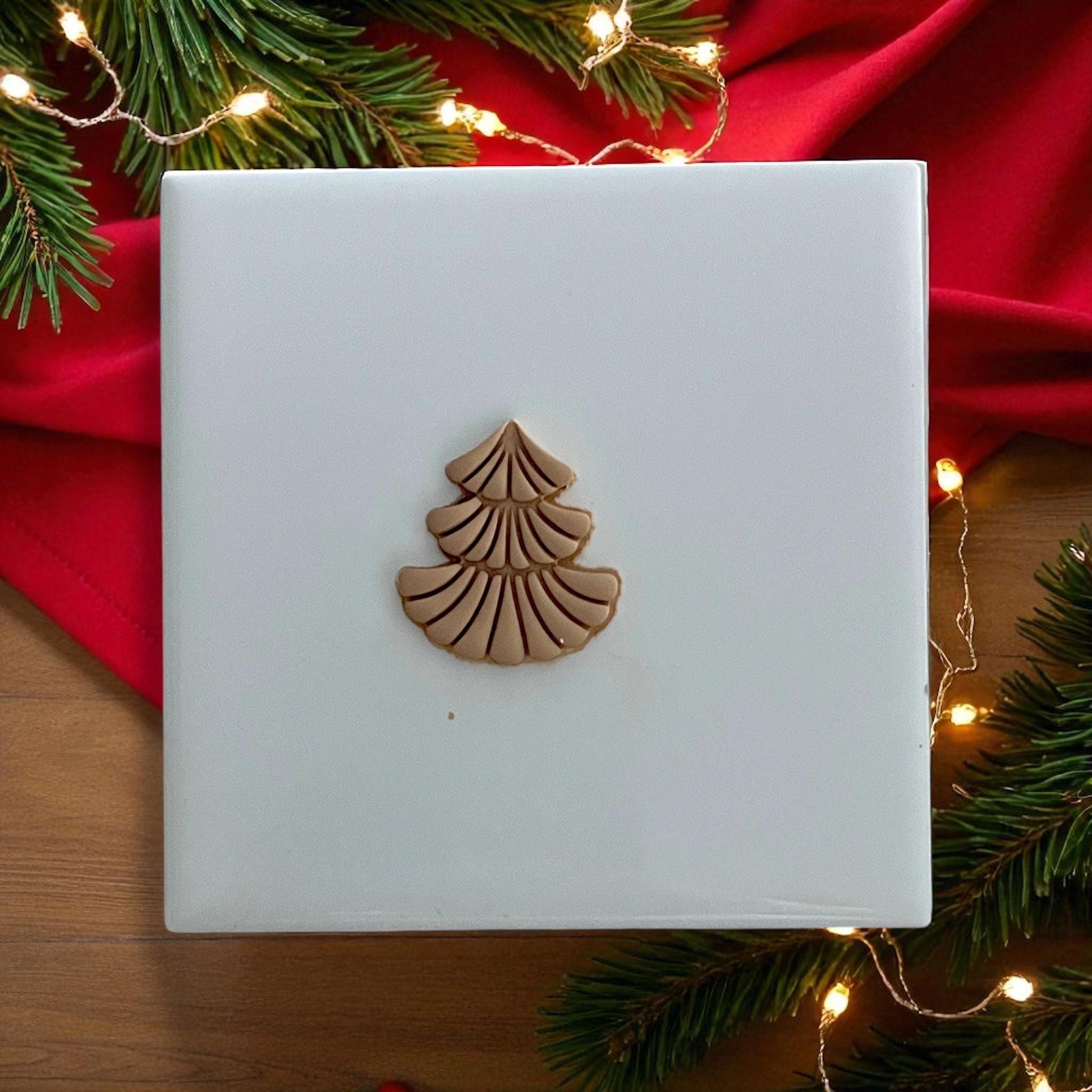 Scalloped Christmas tree polymer clay piece on white tile with Christmas lights and greenery