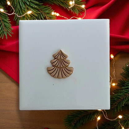 Scalloped Christmas tree polymer clay piece on white tile with Christmas lights and greenery